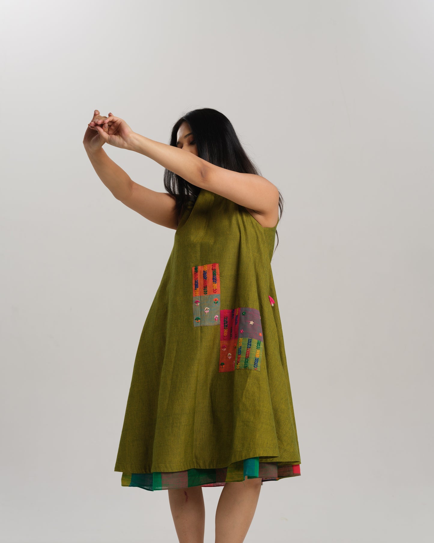 Woman wearing a sleeveless lime green handwoven ikat A-line dress with vibrant patchwork, photographed in a studio setting.
