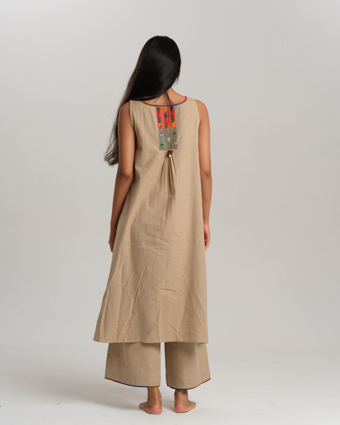 Model wearing beige sleeveless handwoven Ikat kurta set with patchwork in South Indian checks, paired with matching pants and colorful stole – Ikat Rhythm by Taram.