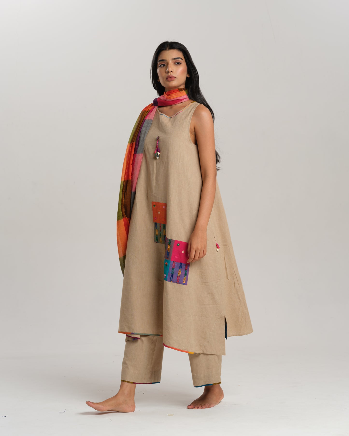 Model wearing beige sleeveless handwoven Ikat kurta set with patchwork in South Indian checks, paired with matching pants and colorful stole – Ikat Rhythm by Taram.