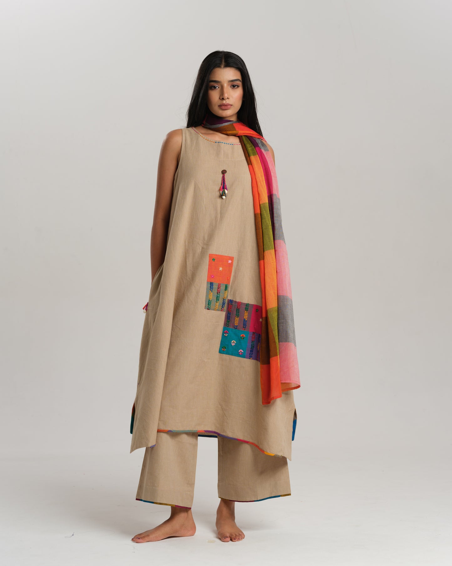 Model wearing beige sleeveless handwoven Ikat kurta set with patchwork in South Indian checks, paired with matching pants and colorful stole – Ikat Rhythm by Taram.