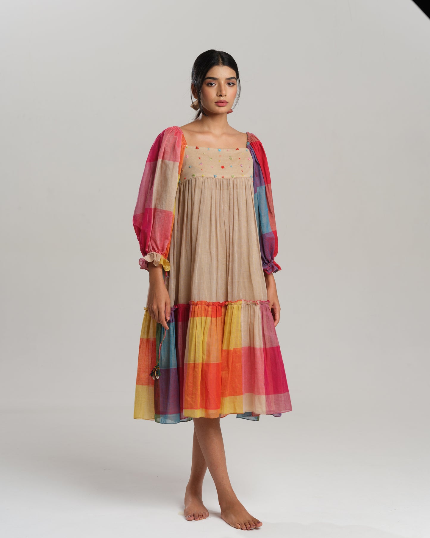 Model wearing a beige cotton Narayanpet dress with colorful puff sleeves and checkered tiers – modern Indian dress for women by Taram.