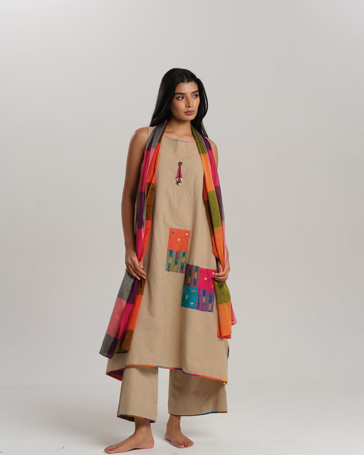 Model wearing beige sleeveless handwoven Ikat kurta set with patchwork in South Indian checks, paired with matching pants and colorful stole – Ikat Rhythm by Taram.