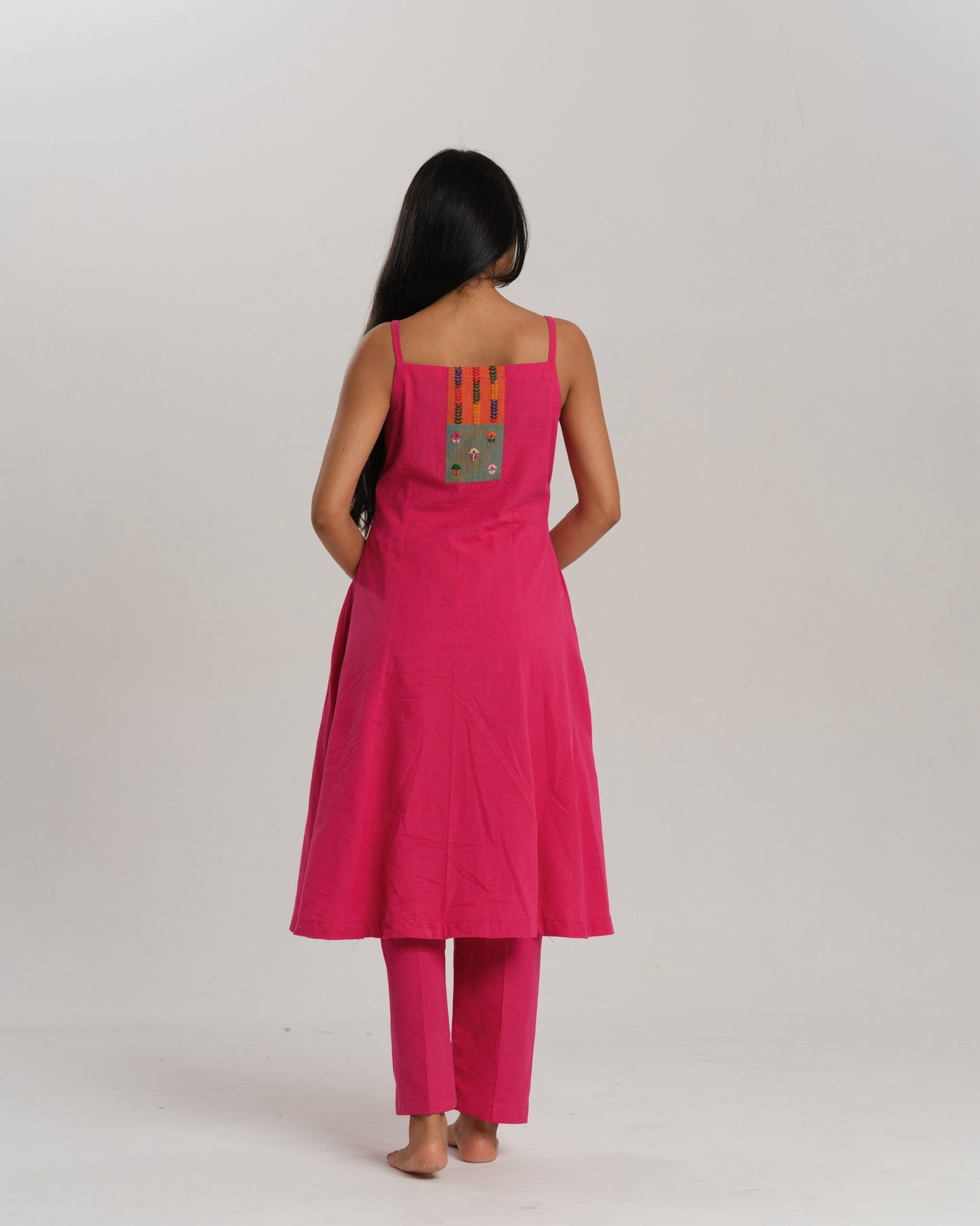 Model wearing a bright pink handwoven kurta set with colourful Ikat patchwork on the yoke, paired with straight pants.