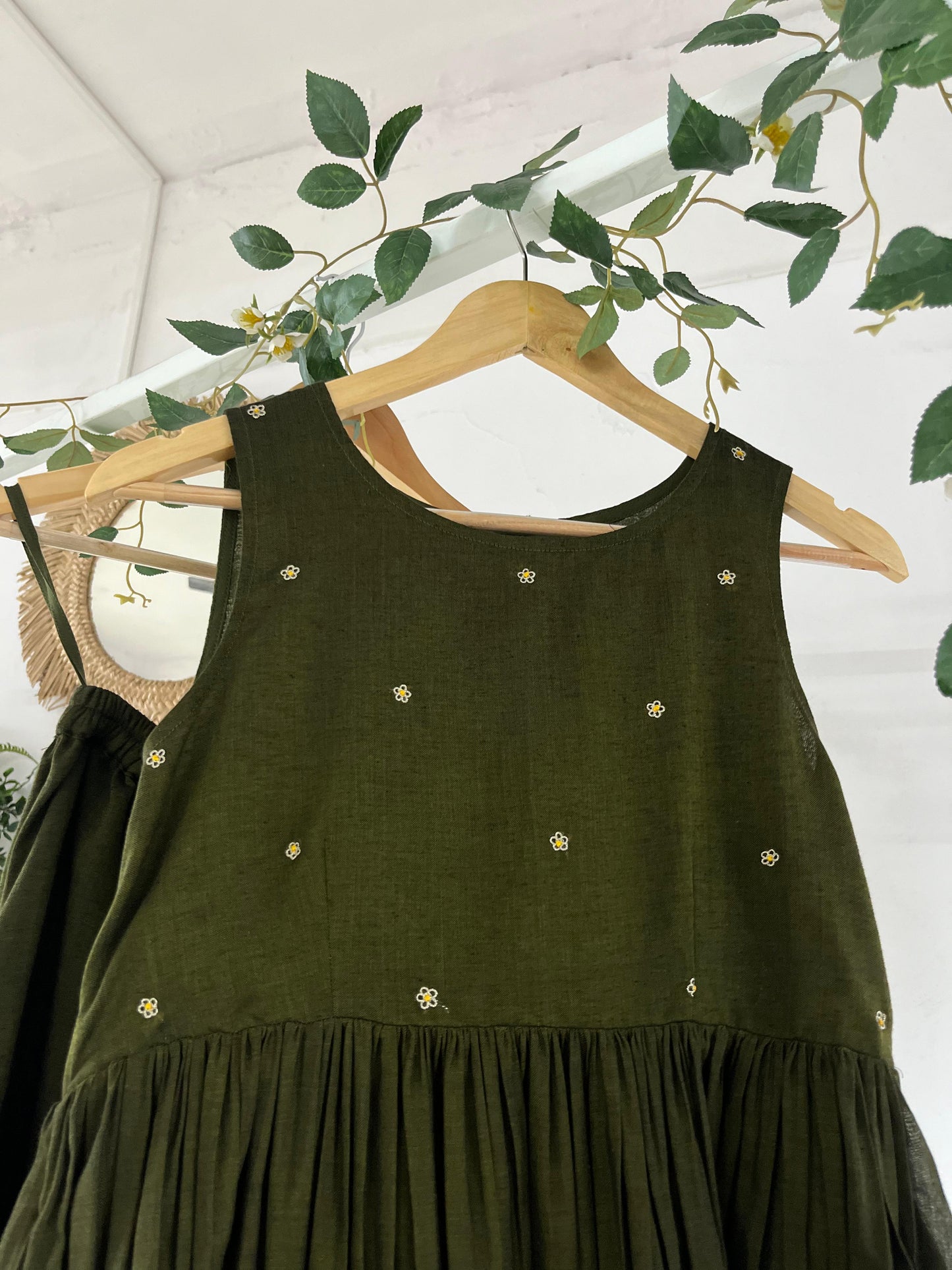 Olive green Narayanpet sharara set with golden zari borders, flared kurta, sharara pants, and dupatta displayed on hangers against a white backdrop with greenery décor.