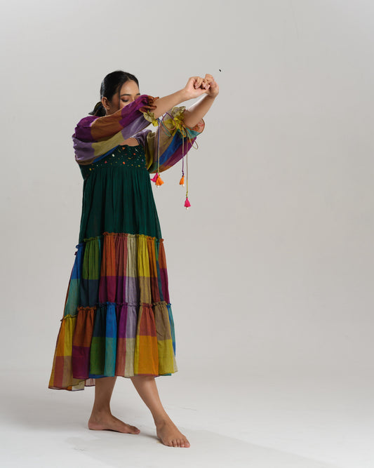 Model wearing a multicoloured handwoven Narayanpet checks cotton tiered dress with puff sleeves and mirror work bodice, styled against a minimalist background.