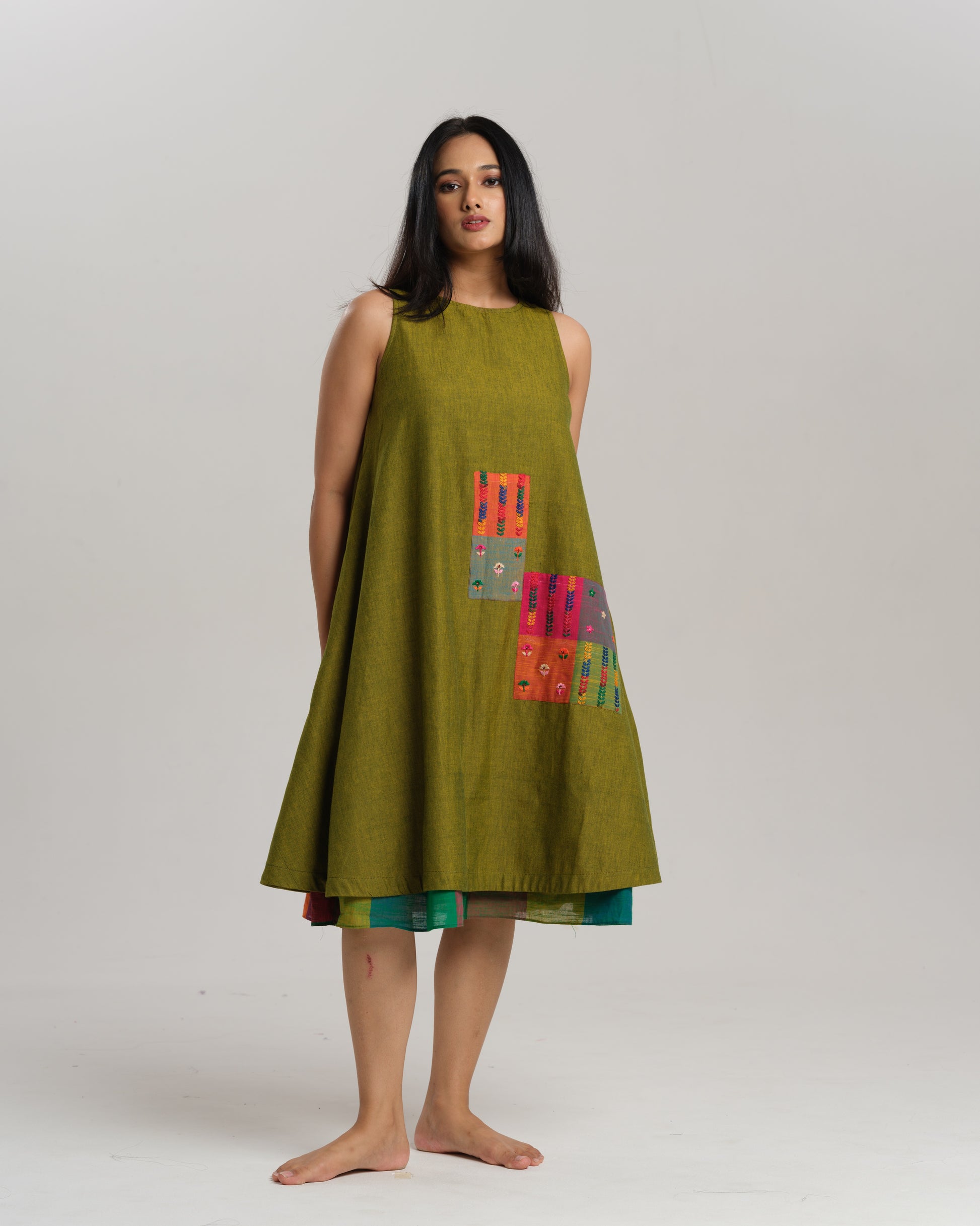 Woman wearing a sleeveless lime green handwoven ikat A-line dress with vibrant patchwork, photographed in a studio setting.