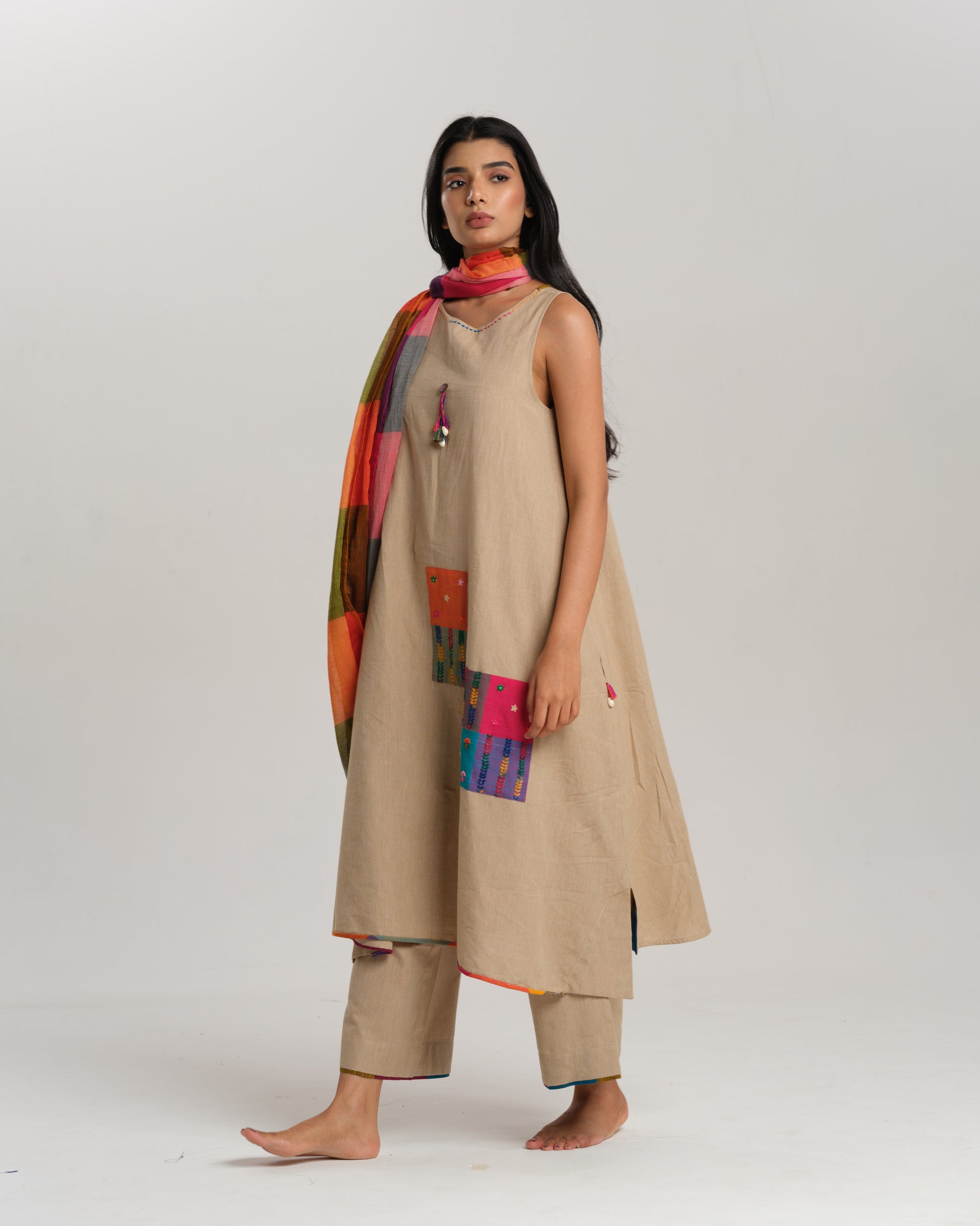 Model wearing beige sleeveless handwoven Ikat kurta set with patchwork in South Indian checks, paired with matching pants and colorful stole – Ikat Rhythm by Taram.