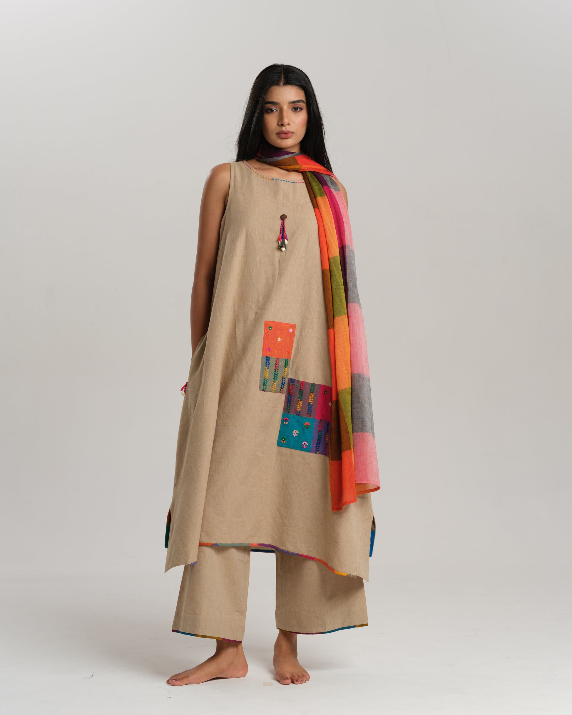 Model wearing beige sleeveless handwoven Ikat kurta set with patchwork in South Indian checks, paired with matching pants and colorful stole – Ikat Rhythm by Taram.