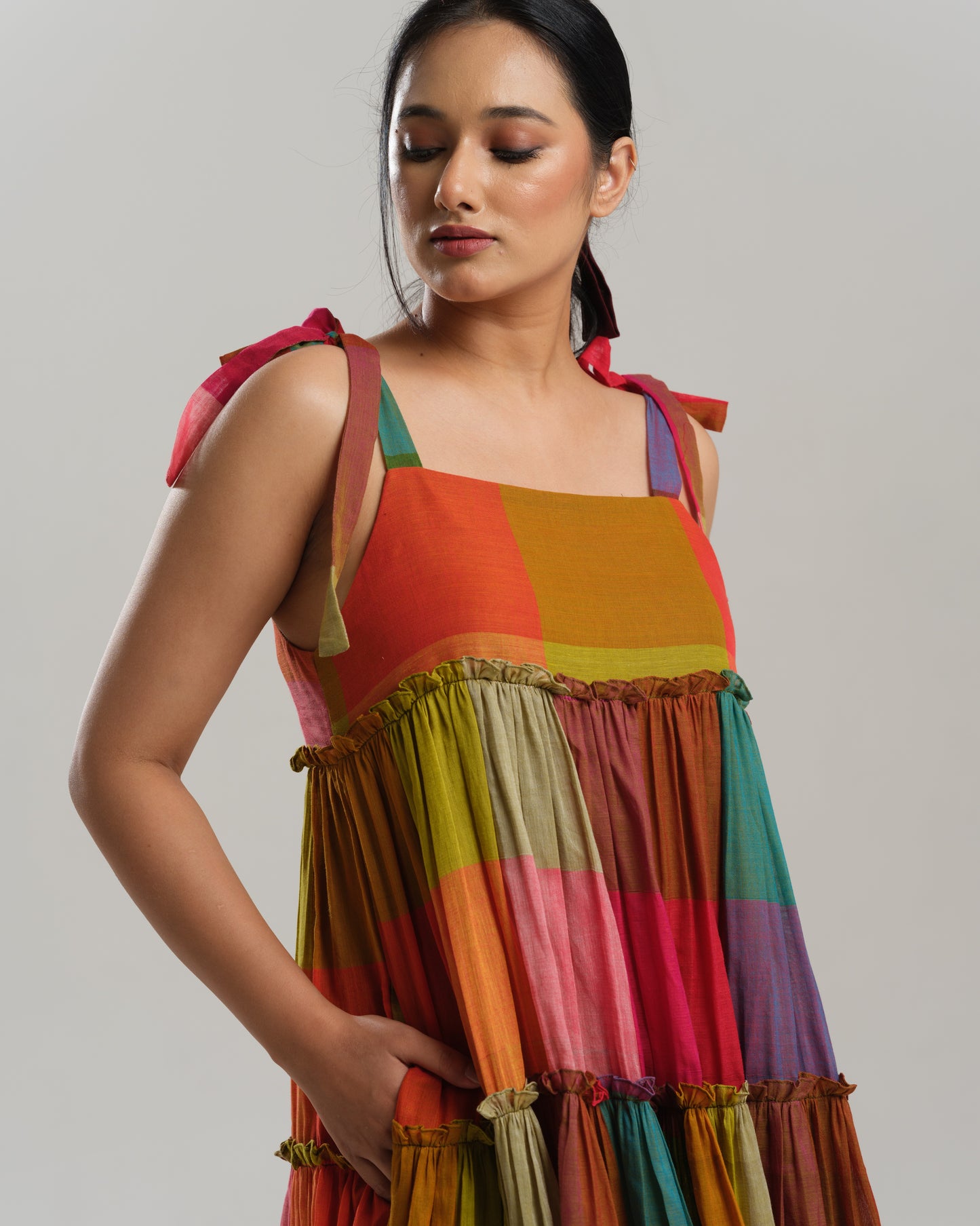 Model wearing a colourful tiered midi dress made from handwoven Narayanpet cotton with multicolour checks and tie-up shoulder straps.