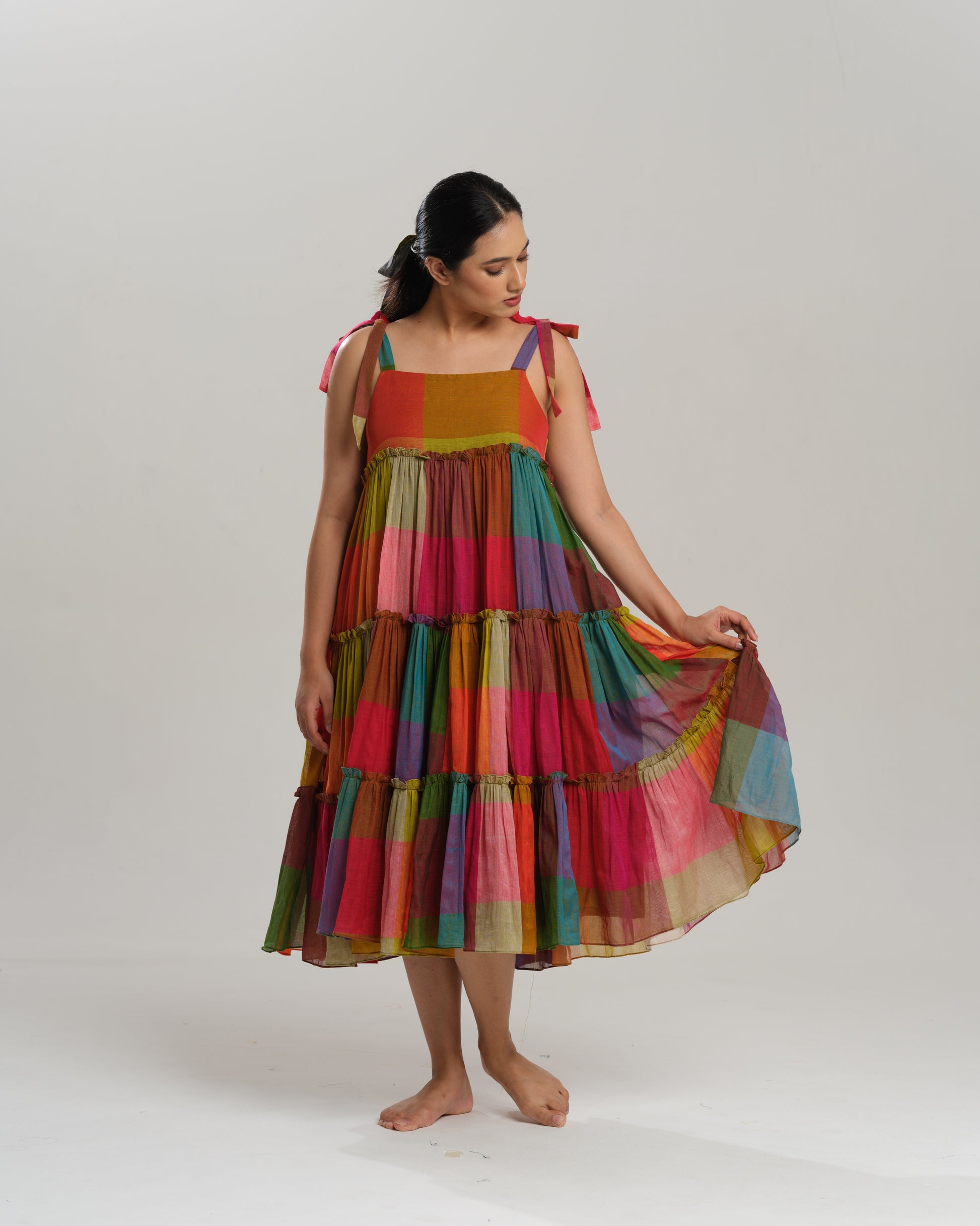 Model wearing a colourful tiered midi dress made from handwoven Narayanpet cotton with multicolour checks and tie-up shoulder straps.