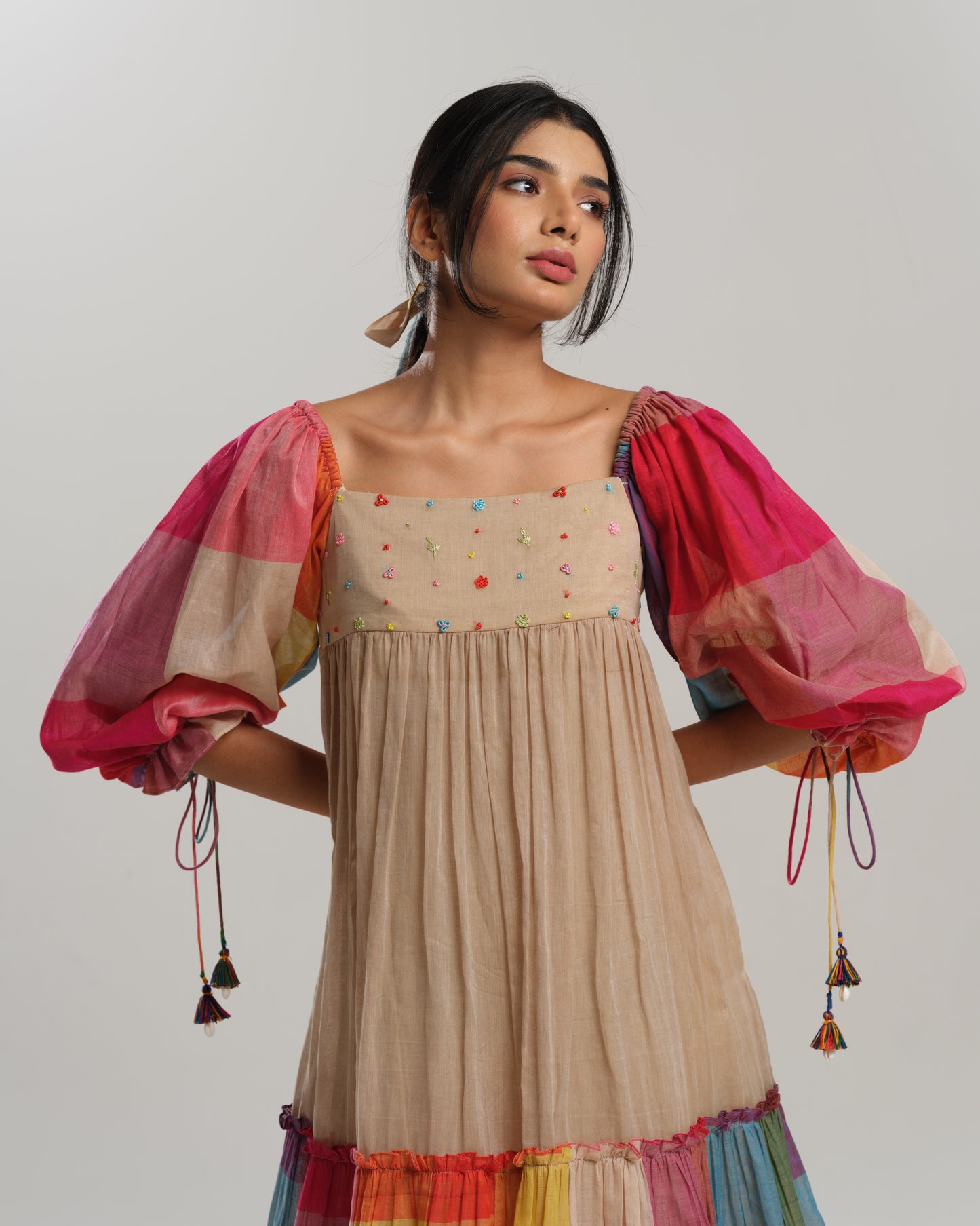 Model wearing a beige cotton Narayanpet dress with colorful puff sleeves and checkered tiers – modern Indian dress for women by Taram.