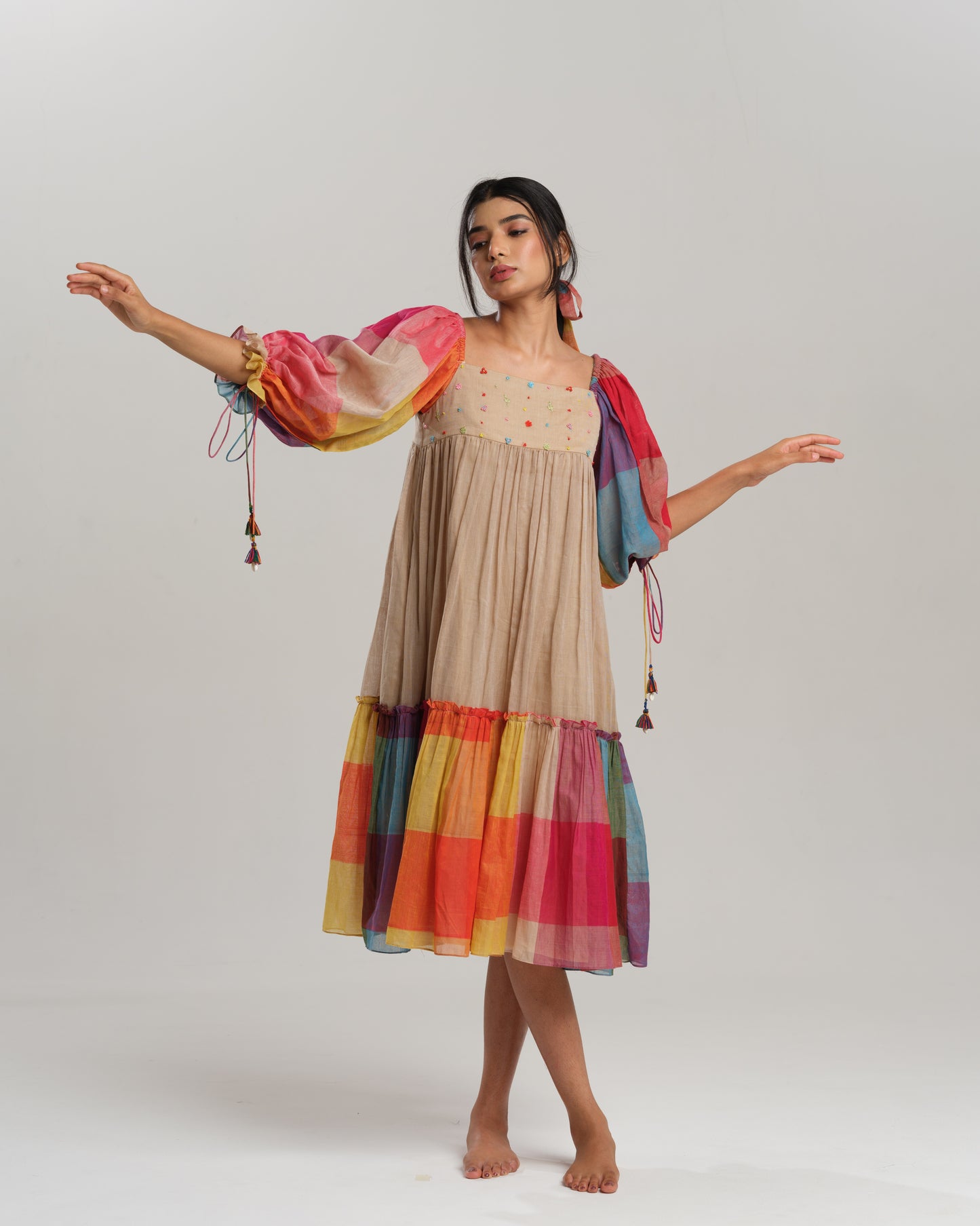 Model wearing a beige cotton Narayanpet dress with colorful puff sleeves and checkered tiers – modern Indian dress for women by Taram.