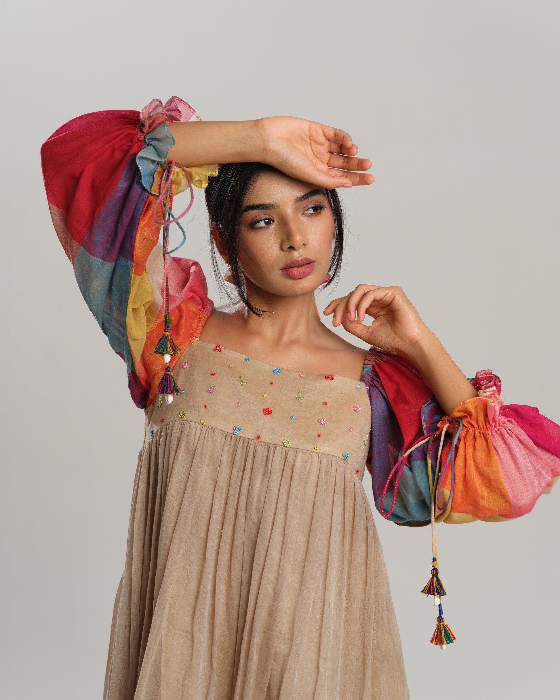 Model wearing a beige cotton Narayanpet dress with colorful puff sleeves and checkered tiers – modern Indian dress for women by Taram.