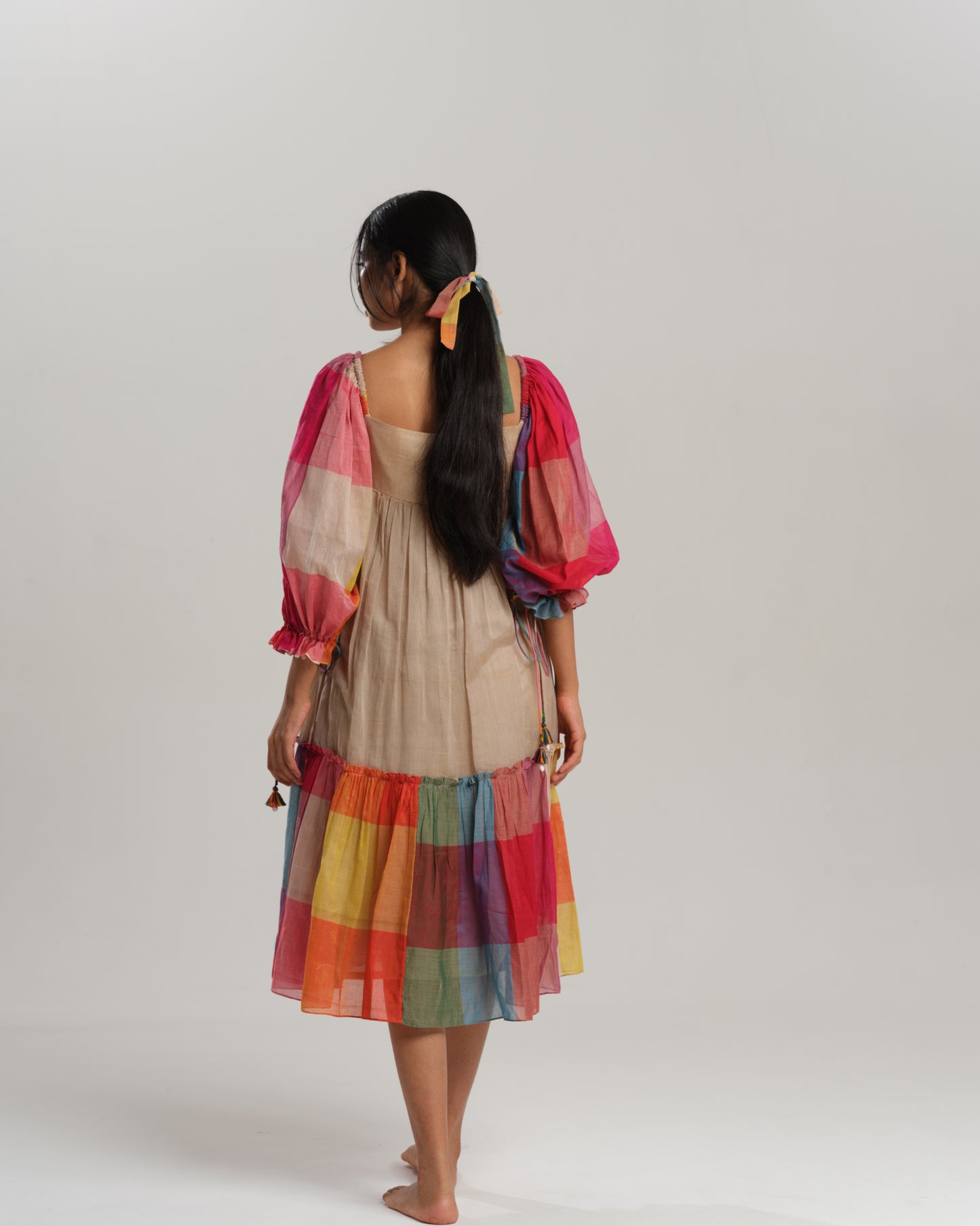 Model wearing a beige cotton Narayanpet dress with colorful puff sleeves and checkered tiers – modern Indian dress for women by Taram.