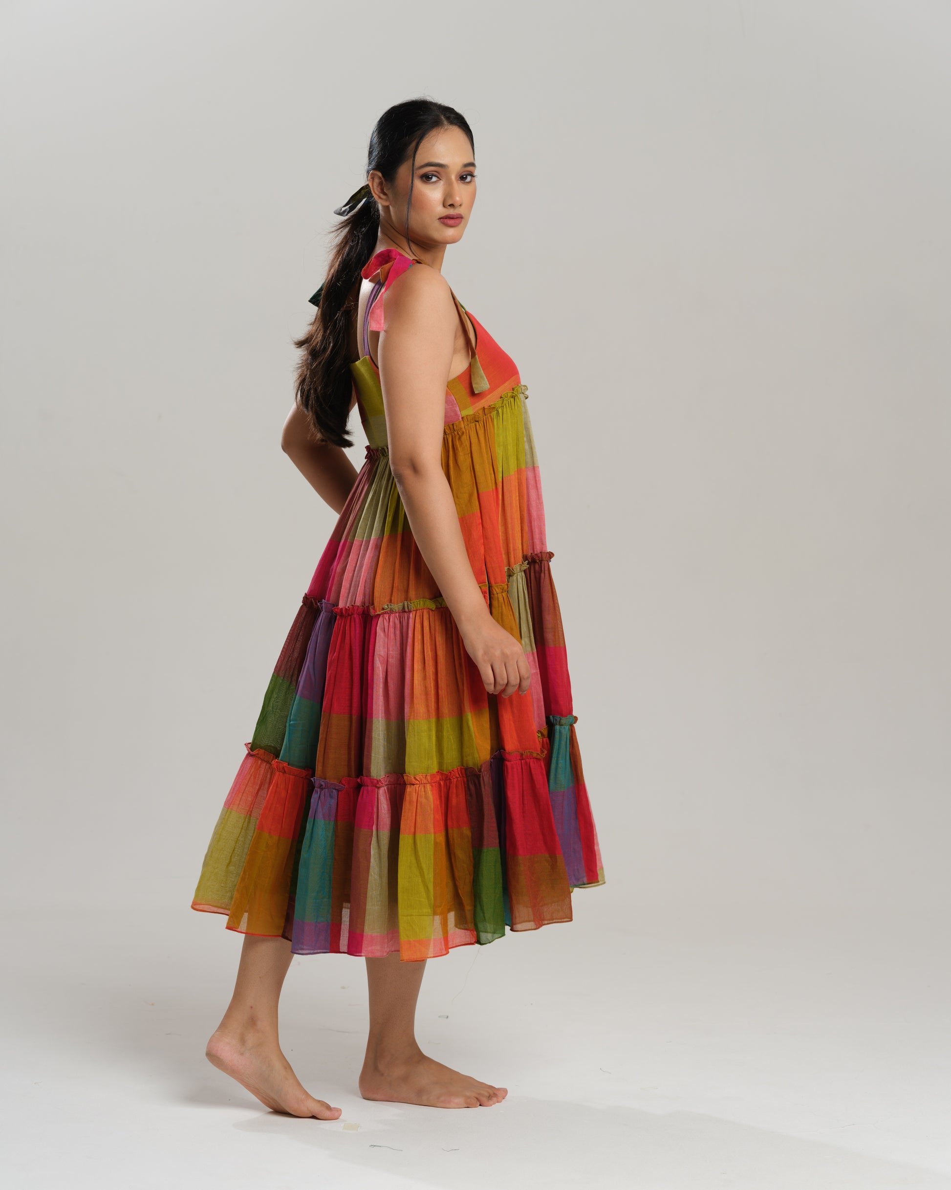 Model wearing a colourful tiered midi dress made from handwoven Narayanpet cotton with multicolour checks and tie-up shoulder straps.