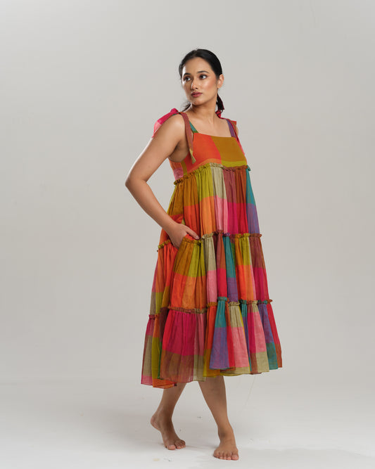 Model wearing a colourful tiered midi dress made from handwoven Narayanpet cotton with multicolour checks and tie-up shoulder straps.