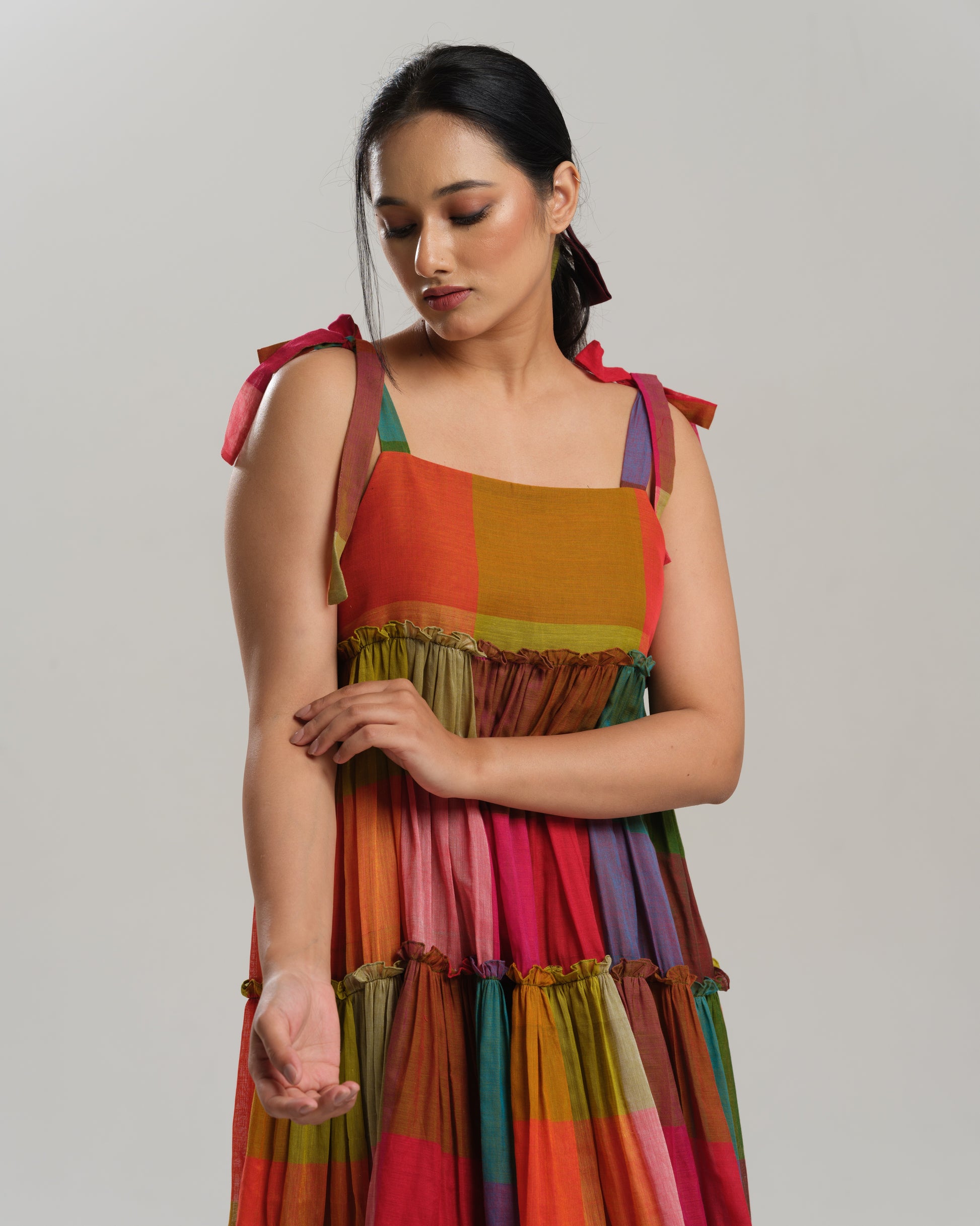 Model wearing a colourful tiered midi dress made from handwoven Narayanpet cotton with multicolour checks and tie-up shoulder straps.