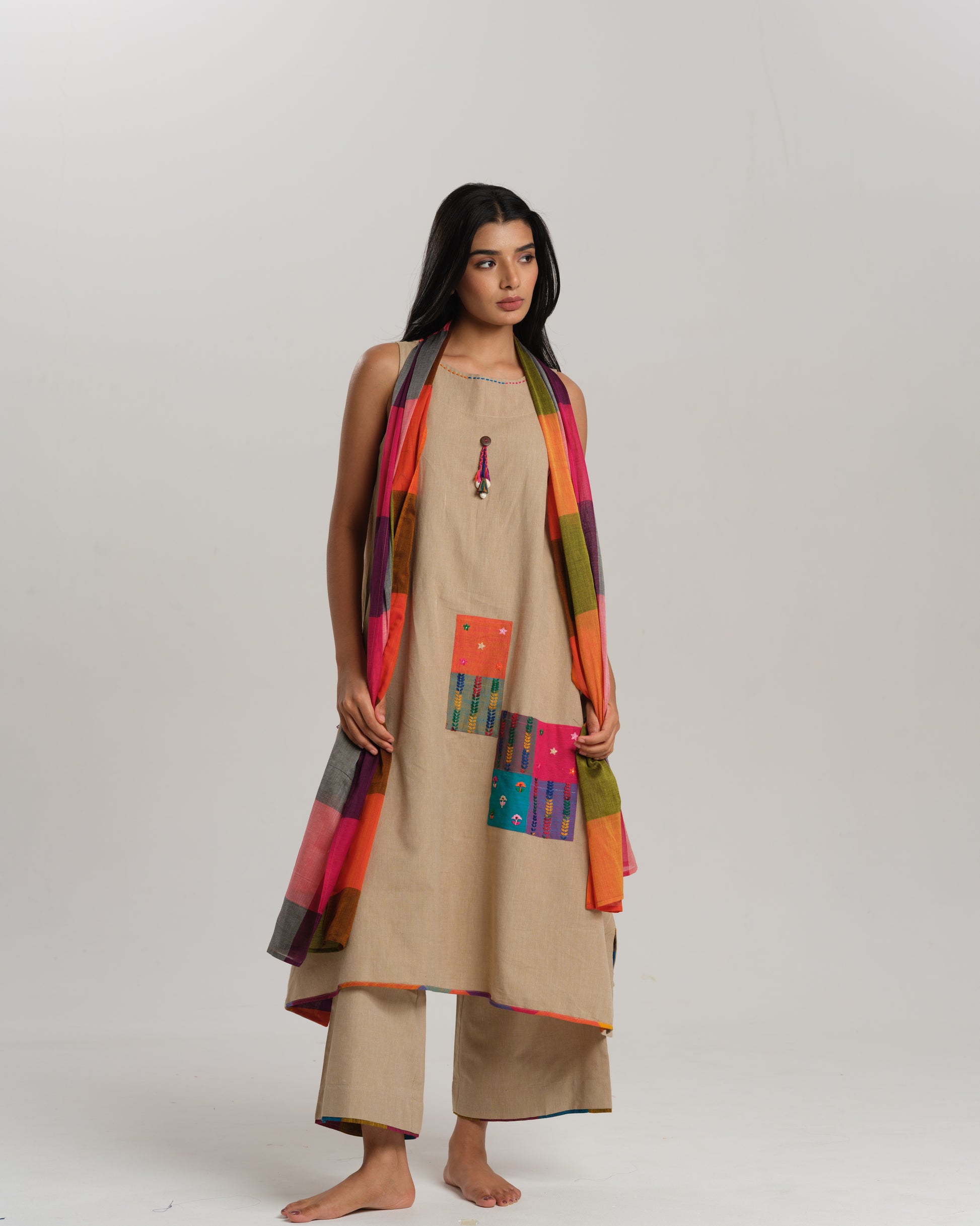 Model wearing beige sleeveless handwoven Ikat kurta set with patchwork in South Indian checks, paired with matching pants and colorful stole – Ikat Rhythm by Taram.