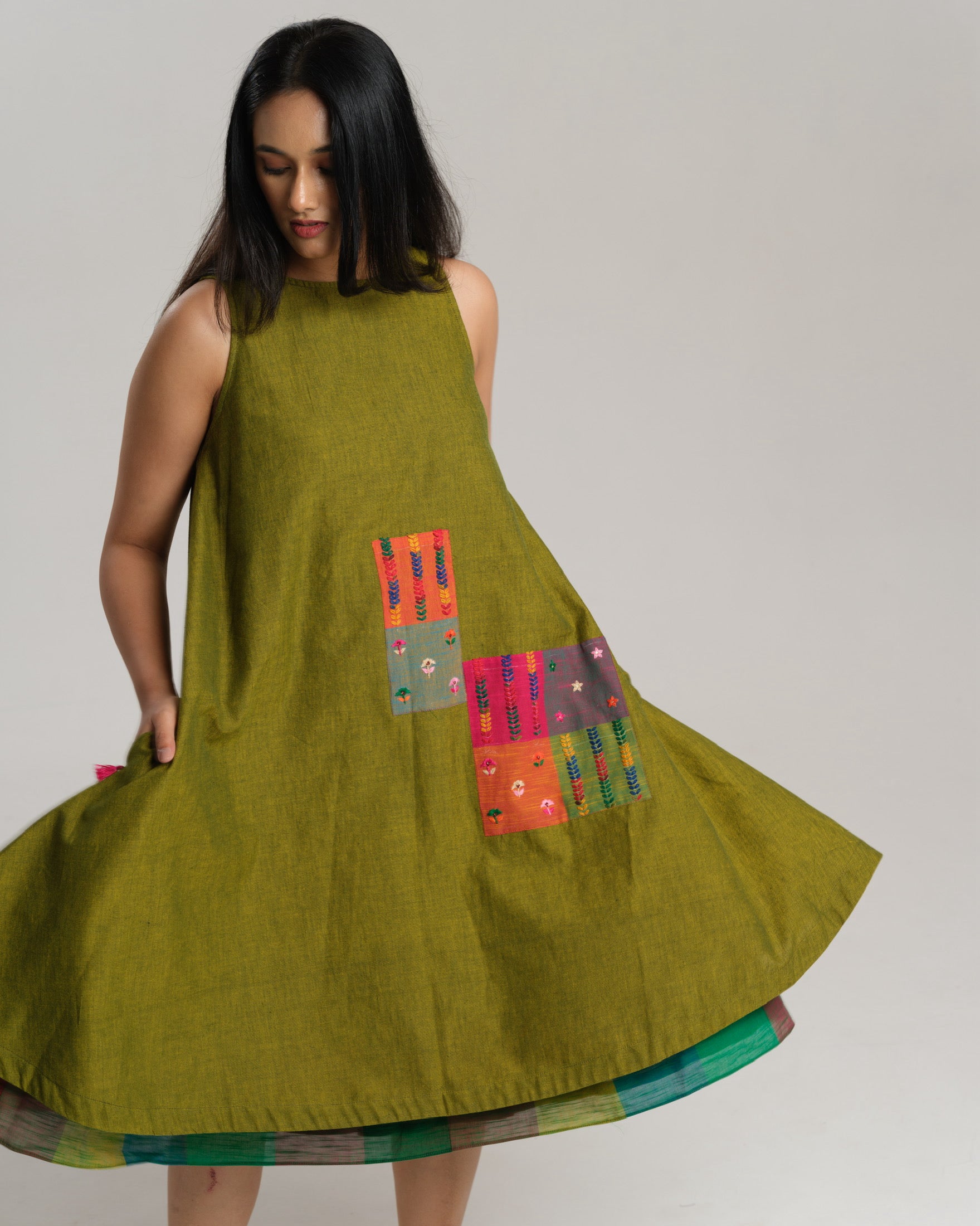 Woman wearing a sleeveless lime green handwoven ikat A-line dress with vibrant patchwork, photographed in a studio setting.