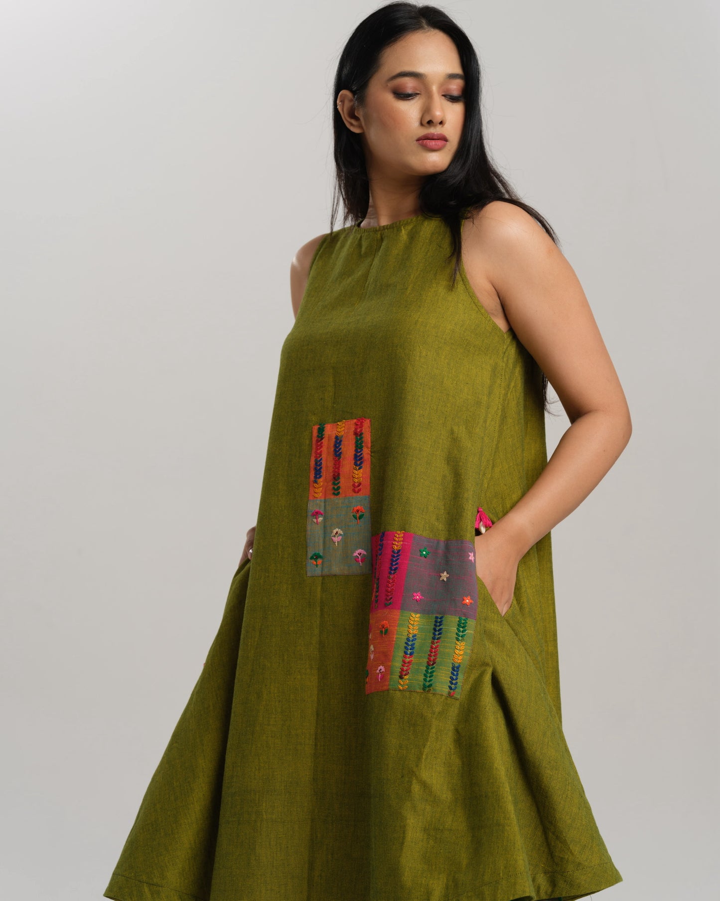 Woman wearing a sleeveless lime green handwoven ikat A-line dress with vibrant patchwork, photographed in a studio setting.