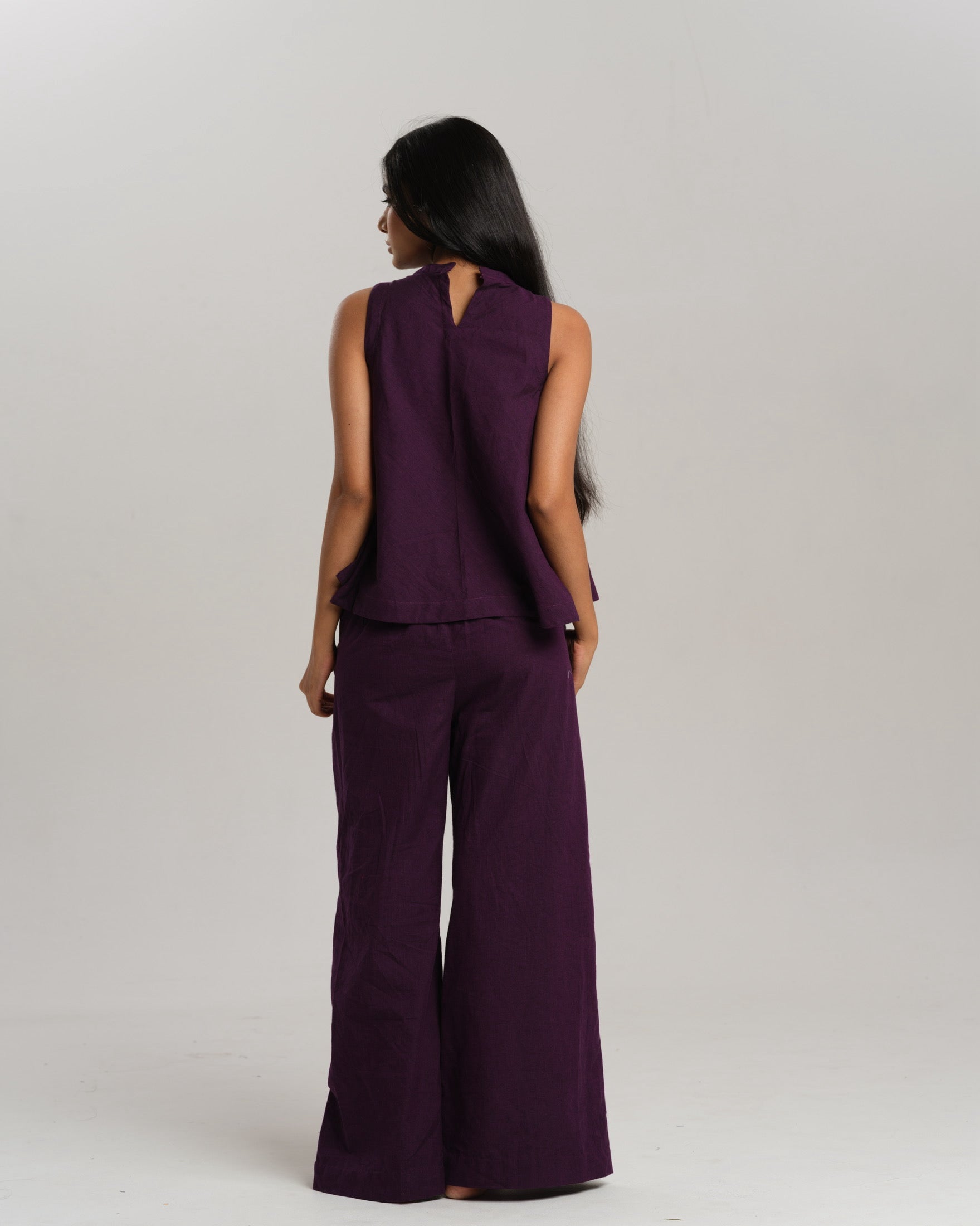 Model wearing a deep plum ikat co-ord set with a sleeveless flared top featuring colourful handwoven ikat patchwork and wide-leg pants, standing barefoot against a neutral background.