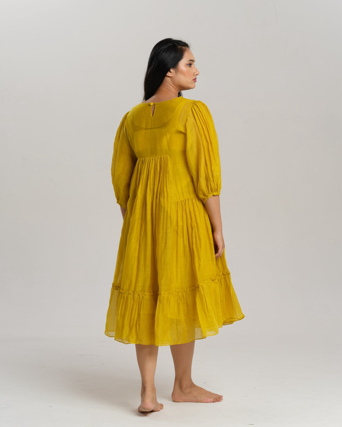 Model wearing a flowy yellow mul Chanderi embroidered dress, holding flowers and standing on green grass.