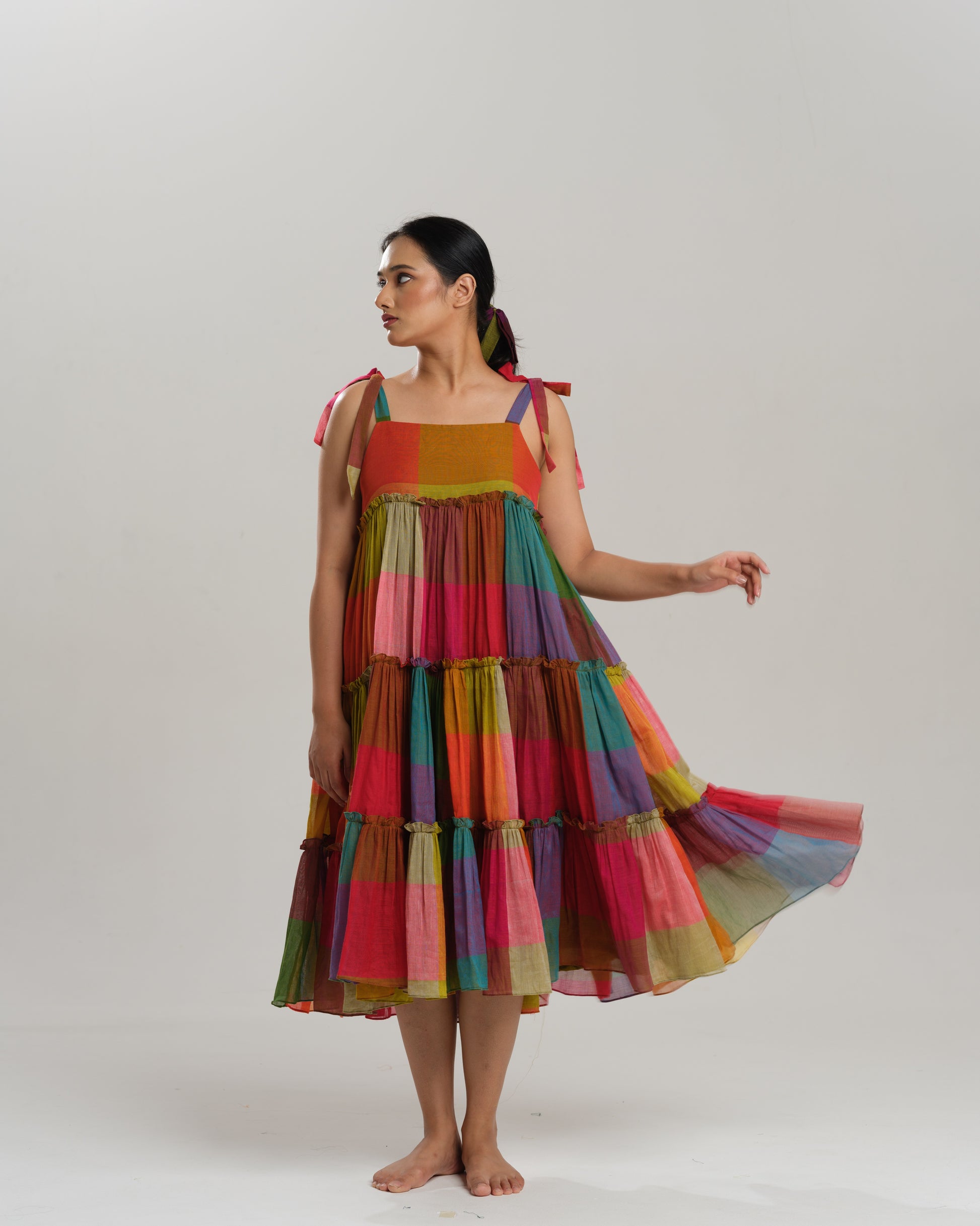 Model wearing a colourful tiered midi dress made from handwoven Narayanpet cotton with multicolour checks and tie-up shoulder straps.
