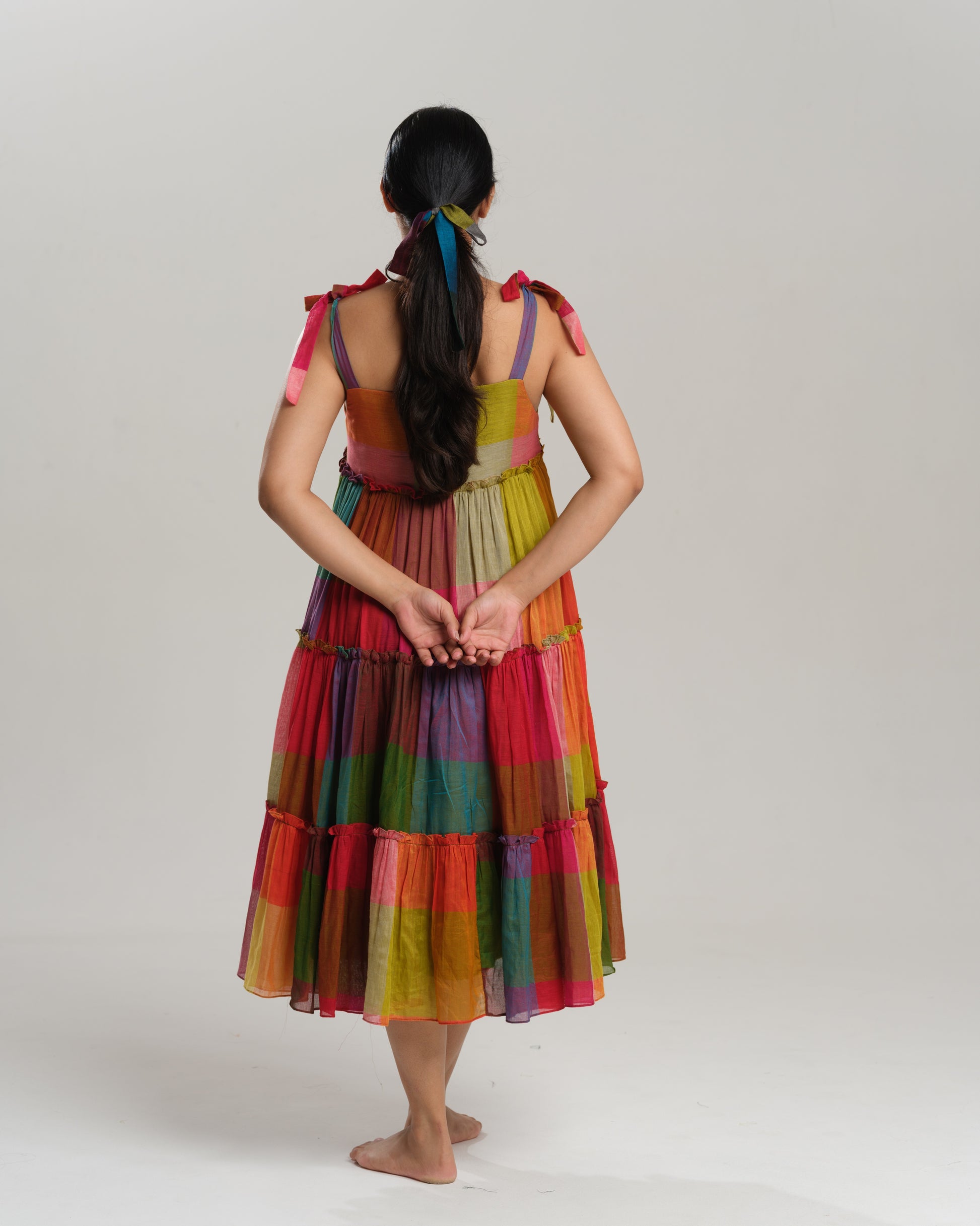 Model wearing a colourful tiered midi dress made from handwoven Narayanpet cotton with multicolour checks and tie-up shoulder straps.