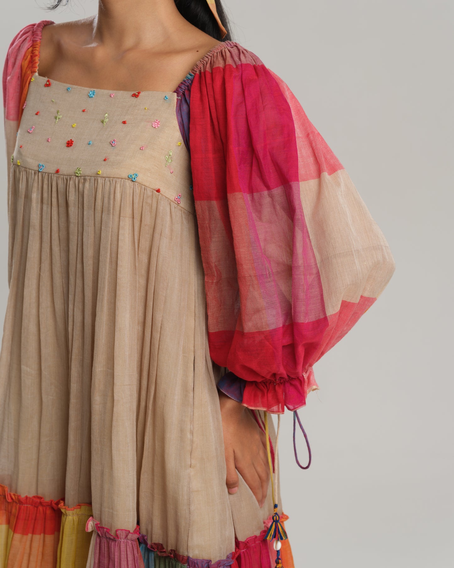 Model wearing a beige cotton Narayanpet dress with colorful puff sleeves and checkered tiers – modern Indian dress for women by Taram.