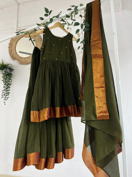 Olive green Narayanpet sharara set with golden zari borders, flared kurta, sharara pants, and dupatta displayed on hangers against a white backdrop with greenery décor.
