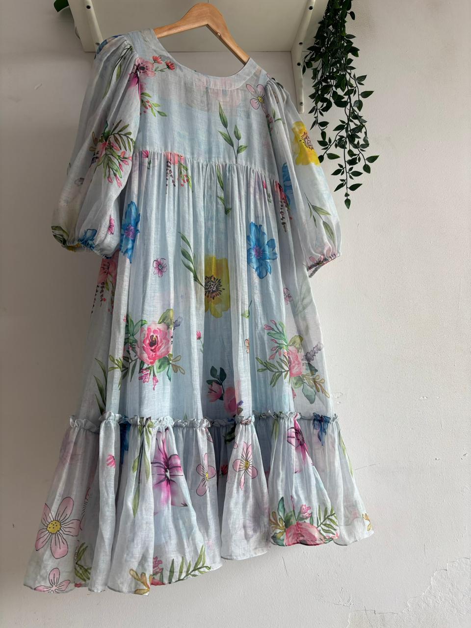 Pastel Meadow Mul Chanderi Multi Tiered Dress with floral patterns, hanging on a wooden hanger.